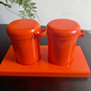 Könnte beinhalten: Ein Set aus zwei leuchtend orangefarbenen Kunststoffbehältern mit Deckeln und Griffen, die auf einem passenden rechteckigen Tablett stehen. Die Behälter haben eine zylindrische Form. Das Set ist wahrscheinlich für die Küche oder den Essbereich bestimmt.