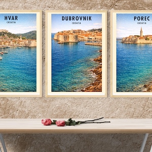 May include: Three framed travel prints featuring coastal scenes of Hvar, Dubrovnik, and Poreč, Croatia. Each print showcases a vibrant blue sea, historic architecture, and the city name. The prints are displayed above a wooden table with roses.
