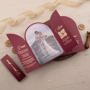 Könnte beinhalten: Burgunderfarbene Hochzeitseinladung mit goldenen Folienakzenten. Die Einladung zeigt ein Foto eines Paares mit den Namen "Ashley & Gabriel" in goldener Schrift. Enthält RSVP, Details und ein Band.