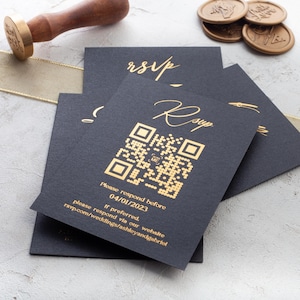 Puede incluir: Tarjetas RSVP negras con texto dorado y un código QR. Las tarjetas incluyen el texto "Please respond before 04/01/2023" y una dirección web. También se ven una cinta dorada, sellos de cera y un sello de madera.