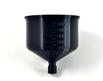 Puede incluir: Embudo negro con una parte superior ancha y una boquilla estrecha. El embudo tiene marcas de medición de 10 a 50. El embudo está hecho de un material sólido y opaco.