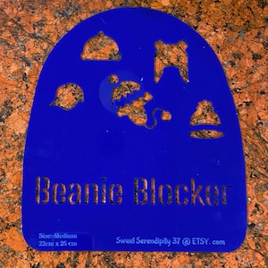 May include: Blue plastic beanie blocker stencil with five cut-out shapes of different hats. The stencil is labeled "Beanie Blocker" and "Size: Medium 22cm x 25cm". The bottom right corner has the text "Sweet Serendipity 37 @ ETSY.com".