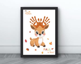 Puede incluir: Impresión artística enmarcada con un ciervo de dibujos animados con cuernos de huellas de manos y el texto "oh, Deer". La obra de arte tiene un tema otoñal con hojas cayendo y la frase "FALL is here!". El ciervo es marrón y blanco.
