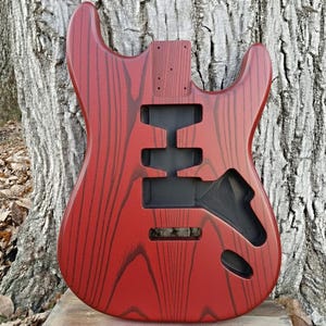 Puede incluir: Cuerpo de guitarra el&eacute;ctrica rojo con acabado de veta de madera. El cuerpo tiene recortes para pastillas, controles y un sistema de tr&eacute;molo. El cuerpo de la guitarra es de madera y tiene un acabado brillante.