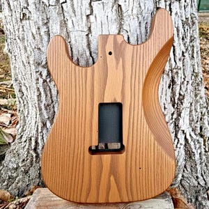 Puede incluir: Una taza de cer&aacute;mica blanca con un asa negra y el texto "But First, Coffee" en negrita negra. La taza se encuentra sobre un fondo borroso, sugiriendo un ambiente acogedor.