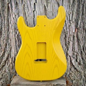 May include: A white ceramic mug with a black handle and the text "But First, Coffee" in a black, handwritten-style font. The mug is on a white surface.