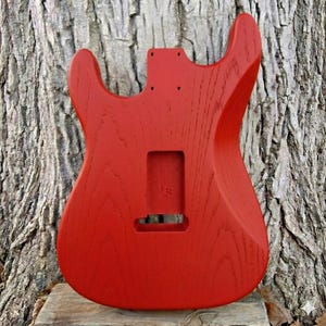 May include: A white ceramic mug with a black handle and the text "But First, Coffee" in a bold, black font. The mug is set against a blurred background, suggesting a cozy setting.