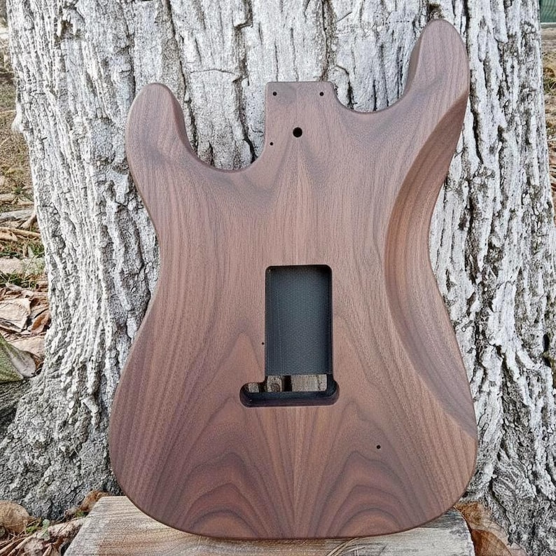 Puede incluir: Cuerpo de guitarra el&eacute;ctrica de madera marr&oacute;n oscuro. El cuerpo tiene una forma contorneada con cortes para acceder a los trastes superiores. Las cavidades de la pastilla y los controles son visibles. La veta de la madera es prominente.