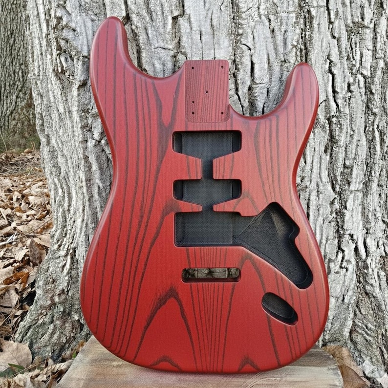 Puede incluir: Cuerpo de guitarra el&eacute;ctrica rojo con acabado de veta de madera. El cuerpo tiene recortes para pastillas, controles y un sistema de tr&eacute;molo. El cuerpo de la guitarra es de madera y tiene un acabado brillante.