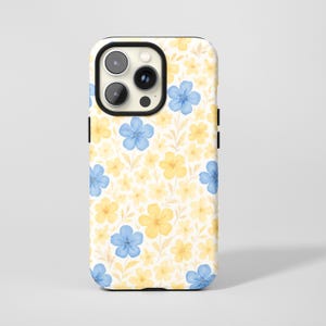 Könnte beinhalten: Eine Handyhülle mit floralem Muster. Das Design umfasst blaue und gelbe Blumen mit hellgelben Blättern auf cremefarbenem Hintergrund. Die Hülle hat einen schwarzen Rahmen um die Kamera und eine schwarze Seitentaste.