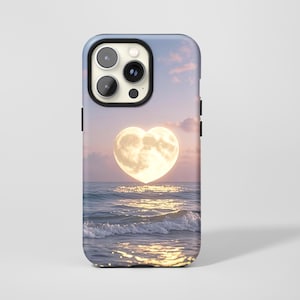 Puede incluir: Una funda para smartphone con un diseño impreso de una luna en forma de corazón brillando sobre un océano tranquilo al atardecer. La escena muestra tonos de cielo rosa y azul suave con olas que reflejan la luz brillante de la luna en el agua.