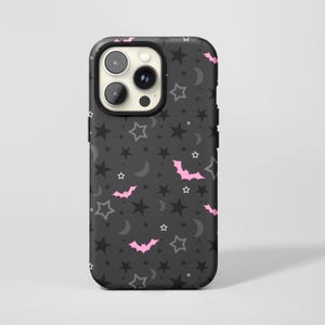 May include: A black phone case with a repeating pattern of pink bats, gray stars, and crescent moons. The case has a black border and a camera cutout.