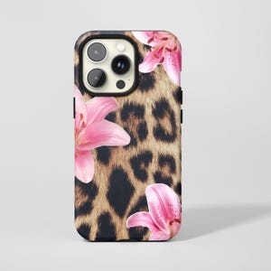 Könnte beinhalten: Schwarze Handyhülle mit Leopardenmuster und rosa Lilienblüten. Die Hülle hat einen schwarzen Rand um die Kamera und eine glänzende Oberfläche. Der Leopardenprint ist braun und schwarz.