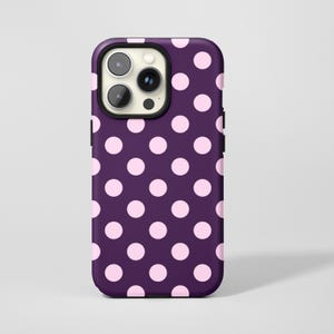 Può includere: Una custodia per telefono con sfondo viola e un motivo a pois rosa chiaro uniformemente distanziati. La custodia ha un bordo nero attorno agli obiettivi della fotocamera.