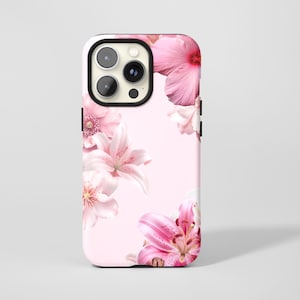May include: A phone case with a pink floral design. The case has a light pink background with various pink flowers, including lilies and hibiscus. The phone's camera lenses are visible at the top.