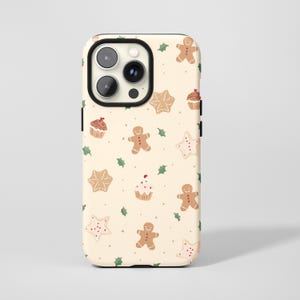 May include: A phone case with a festive pattern of gingerbread men, star-shaped cookies, and cupcakes on a cream background. Green holly leaves and small dots complete the holiday design.