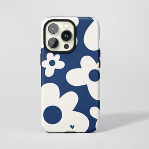 Könnte beinhalten: Eine marineblaue und weiße Handyhülle mit einem floralen Muster. Die Hülle hat einen weißen Rand und einen marineblauen Hintergrund mit großen weißen Blumenformen. Unten befindet sich ein kleines Herz. Die Kameralinsen des Telefons sind oben sichtbar.