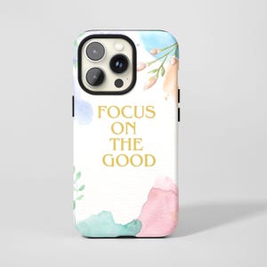 May include: A white phone case with a watercolour design and the text "FOCUS ON THE GOOD" in gold. The case features pastel blue, pink, and green watercolour splotches and floral accents. The phone case has a black camera cutout.