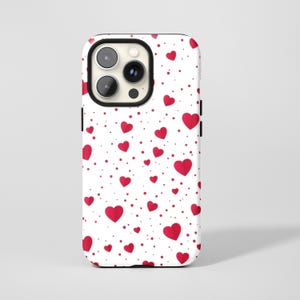 Op de afbeelding: Een witte telefoonhoes met een patroon van rode harten en kleine rode stippen. De hoes heeft een zwarte cameramodule en zwarte zijknoppen. Het ontwerp heeft een romantisch en speels thema.