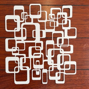 May include: White geometric design with a series of interlocking squares and rectangles. The design is cut out of a single piece of paper and is reminiscent of mid-century modern art.