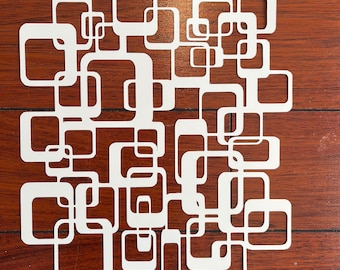 May include: White geometric design featuring a series of interlocking squares and rectangles. The design is cut out from a single piece of paper and evokes a mid-century modern aesthetic.