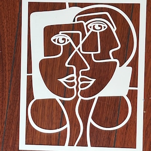May include: White paper cut-out art depicting two abstract faces with overlapping features. The faces are outlined in black and have simple eyes, noses, and mouths.