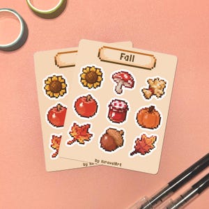 May include: Two sticker sheets with pixelated fall-themed illustrations, including a sunflower, apple, mushroom, pumpkin, and leaves. The word "Fall" is at the top of the sheet. The artist's name is at the bottom.