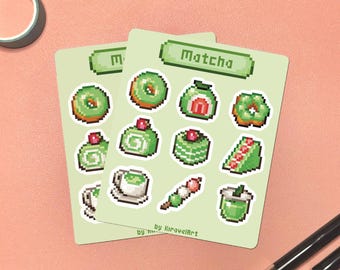 May include: Two light green sticker sheets with pixelated matcha-themed illustrations. The stickers include donuts, sushi, and other Japanese sweets. The word "Matcha" is at the top of the sheet. Pens and washi tape are in the background.