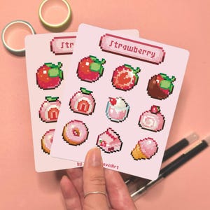 May include: Two pink cards with pixelated strawberry-themed illustrations. The cards feature various strawberry designs, including whole strawberries, desserts, and ice cream. The word "Strawberry" is written at the top of one card.