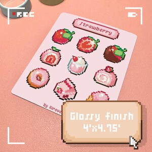 May include: A pink sticker sheet featuring pixelated strawberry-themed illustrations of various desserts. The sheet includes the word "Strawberry" and the text "by Kiraye". The sticker sheet has a glossy finish and measures 4" x 4.75".