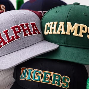 Arched college embroidery font stitched in 3D puff foam style on flat brim snapback hat