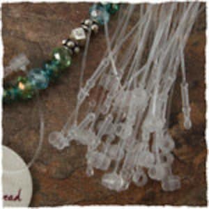 May include: A close-up of a pile of clear plastic string ties with a small loop at one end. The ties are used for attaching price tags to items.