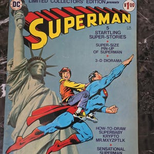 Puede incluir: Una portada de cómic vintage de Superman con Superman volando con un niño, la Estatua de la Libertad y la palabra "SUPERMAN". La portada es una edición limitada de coleccionista con un precio de $1.00.