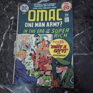 May include: Vintage DC Comics' "OMAC" comic book cover. The cover features vibrant illustrations of a superhero, villains, and text. The comic book is titled "OMAC One Man Army?" and includes the text "Mister Big Can Rent a City! For Assassination!"