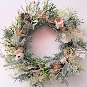 May include: A coastal-themed wreath featuring a variety of seashells, starfish, and sea urchins. The wreath is adorned with green and gray faux foliage, creating a natural and textured appearance. The wreath is approximately 16 inches in diameter.
