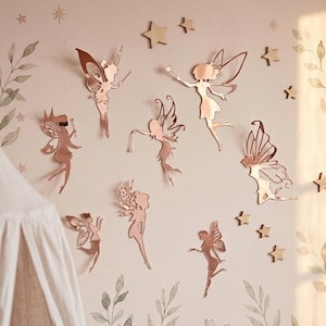 Pu&ograve; includere: Decalcomanie da parete a forma di fata in oro rosa e stelle in legno adornano una parete rosa chiaro. Le fate, con intricati disegni alari, sono in varie pose. La parete &egrave; decorata con motivi floreali e di foglie ad acquerello, creando un tema per la cameretta.