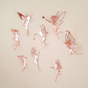 Pu&ograve; includere: Una collezione di otto decorazioni murali a forma di fata in oro rosa in varie pose. Ogni fata ha ali dettagliate ed &egrave; tagliata da un metallo riflettente. Alcune fate tengono bacchette, il tutto su uno sfondo neutro.