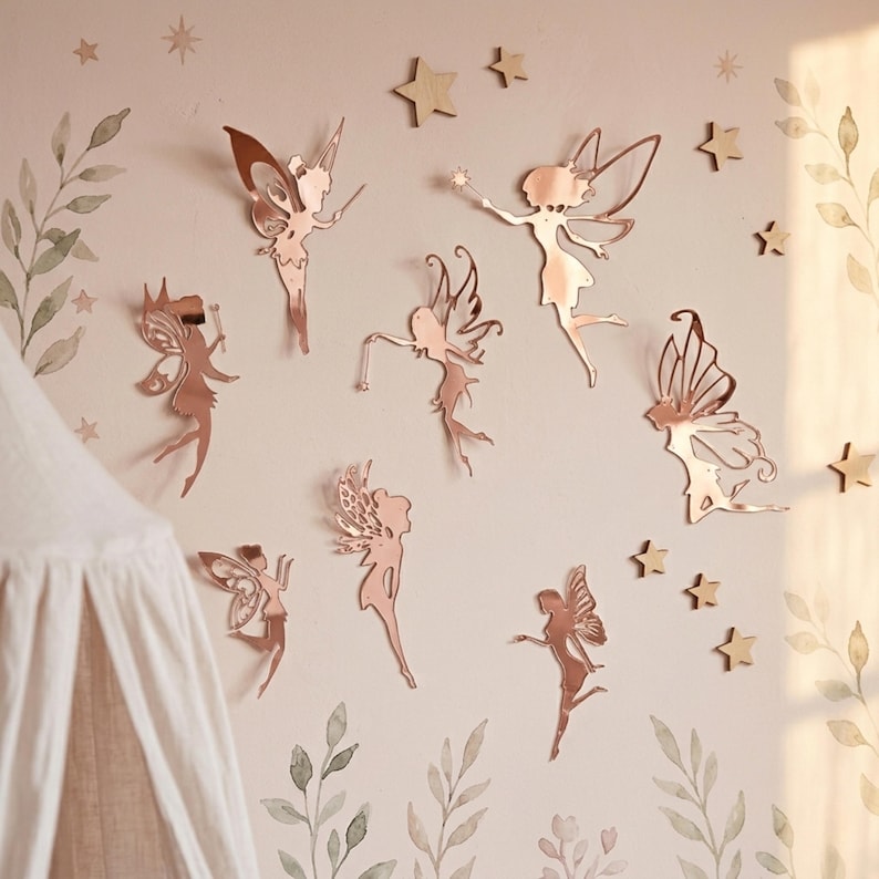 Pu&ograve; includere: Decalcomanie da parete a forma di fata in oro rosa e stelle in legno adornano una parete rosa chiaro. Le fate, con intricati disegni alari, sono in varie pose. La parete &egrave; decorata con motivi floreali e di foglie ad acquerello, creando un tema per la cameretta.
