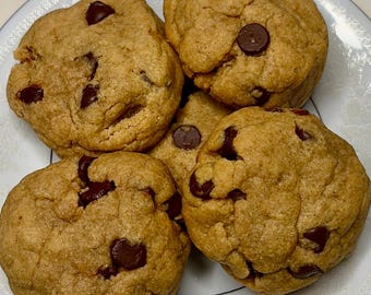 May include: A plate of five freshly baked chocolate chip cookies. The cookies are golden brown with visible chocolate chips throughout. The plate has a white and light blue floral design around the rim.