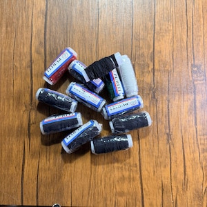 May include: A collection of spools of thread in various colors, including red, black, and white, arranged on a wooden surface. The spools are labeled with the word "PURITI".