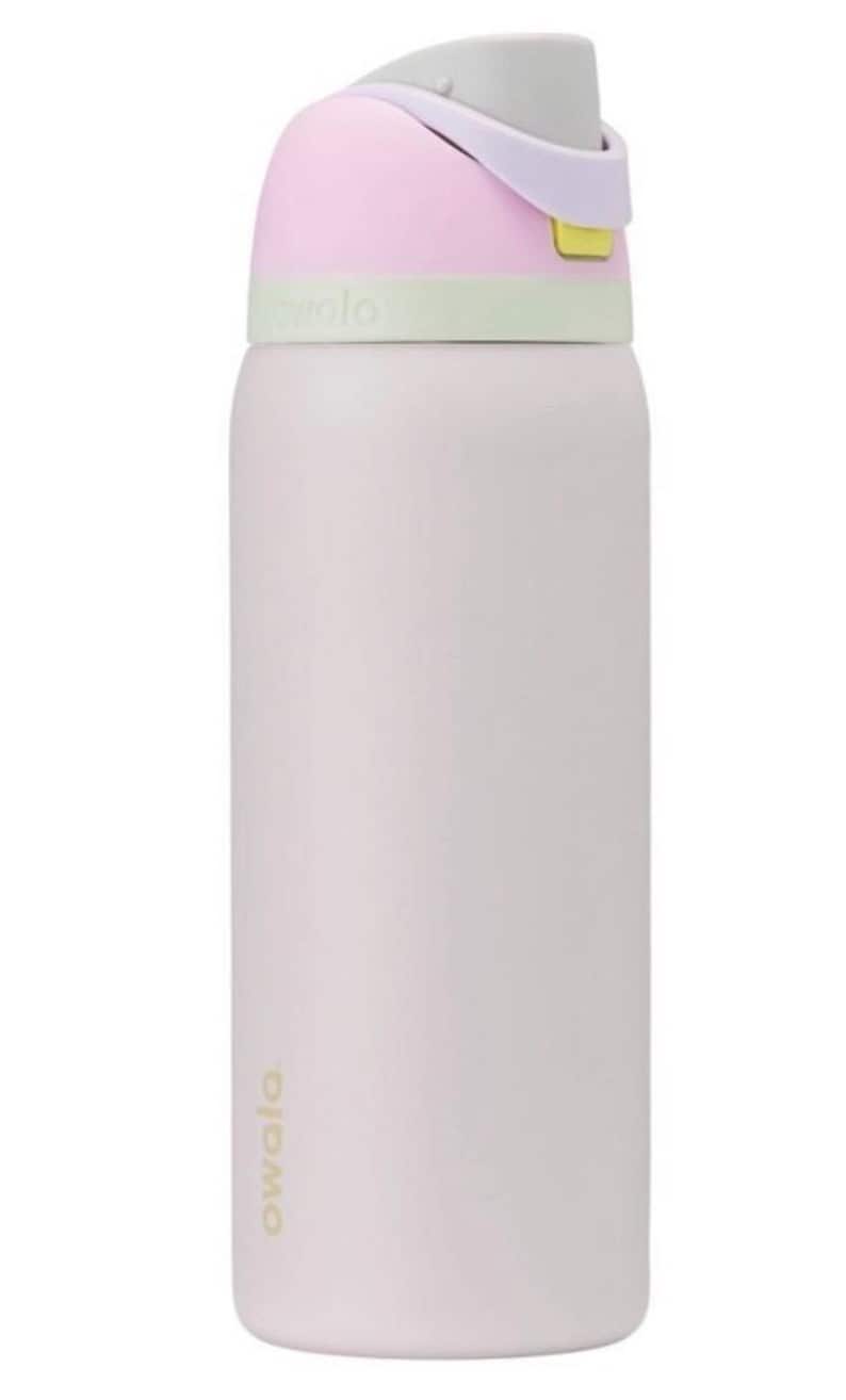 May include: A pastel-colored Owala water bottle. The bottle is primarily a light pink with a white body. The lid is a combination of pink, gray, and green. The bottle has a flip-top lid and a handle. The word "owala" is printed on the bottle.
