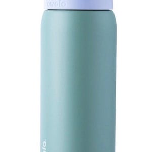 May include: A teal-colored water bottle with a white and purple lid. The bottle has the brand name "owala" printed on it. The bottle is cylindrical and appears to be made of metal or a similar material. The lid has a built-in handle.
