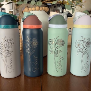May include: Six colorful water bottles with floral designs and names. Each bottle has a different color lid and base, with names like "Erin" and "Staci" in script. The bottles are on a wooden surface.
