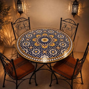 Puede incluir: Una mesa redonda con un tablero de mosaico geométrico en azul, amarillo y blanco y una estructura de metal negro, acompañada de tres sillas de metal negro con respaldos de volutas y cojines de asiento naranjas lisos.
