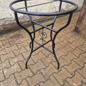 May include: Black metal side table with a circular top and decorative heart-shaped accents. The table has a sturdy, four-legged base and an open design. The table's height is approximately 61 cm.