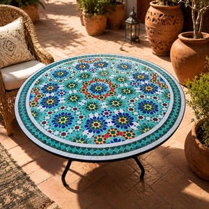 Peut inclure: Une table ronde dotée d'un plateau en mosaïque aux motifs géométriques en étoile complexes dans des tons turquoise, bleu, jaune, rouge et blanc. La table est soutenue par un cadre en métal noir simple avec des pieds incurvés et une bordure.