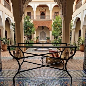 Puede incluir: Una base de mesa de metal negro que presenta un marco superior rectangular y una estructura de soporte en forma de X con un elemento decorativo central de volutas. El marco está construido con varillas de metal oscuro y se apoya sobre cuatro patas curvas.