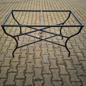 May include: A dark gray metal table frame with a rectangular top and curved legs. The frame features an ornate heart-shaped design in the center. The table frame is designed to support a tabletop, and is suitable for outdoor or indoor use.
