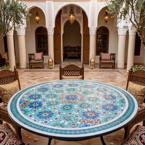 May include: A round mosaic tile table with a black metal base. The tabletop features a turquoise, blue, and white floral pattern. The table is surrounded by wooden chairs with patterned cushions, in an outdoor courtyard setting.