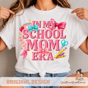 Può includere: Una t-shirt bianca con un design grafico che riporta il testo IN MY SCHOOL MOM ERA in lettere rosa. Il design include illustrazioni di un quaderno rosa, un fiocco a quadri color ottanio, un grande fiocco rosa, un paio di forbici e pastelli gialli e viola.